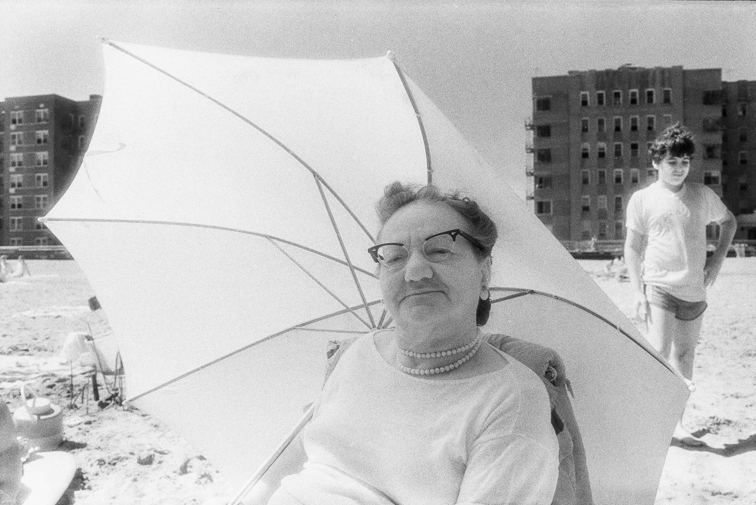Barbara Alper- Photo of women sitting under an umbrella on Rockaway Beach NYC