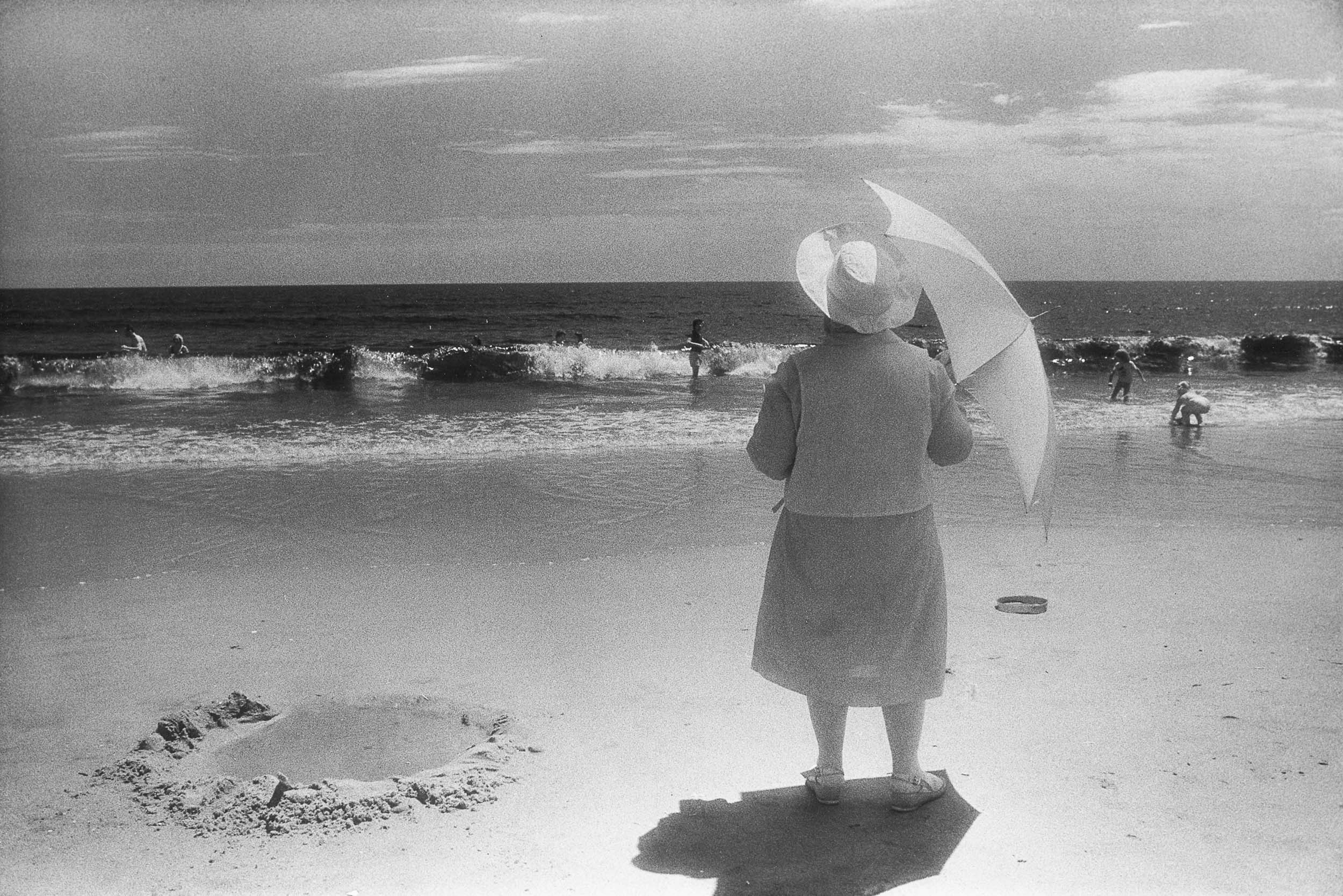Barbara Alper- Photo of women holding an umbrella while watching the waves at Rockaway Beach NYC
