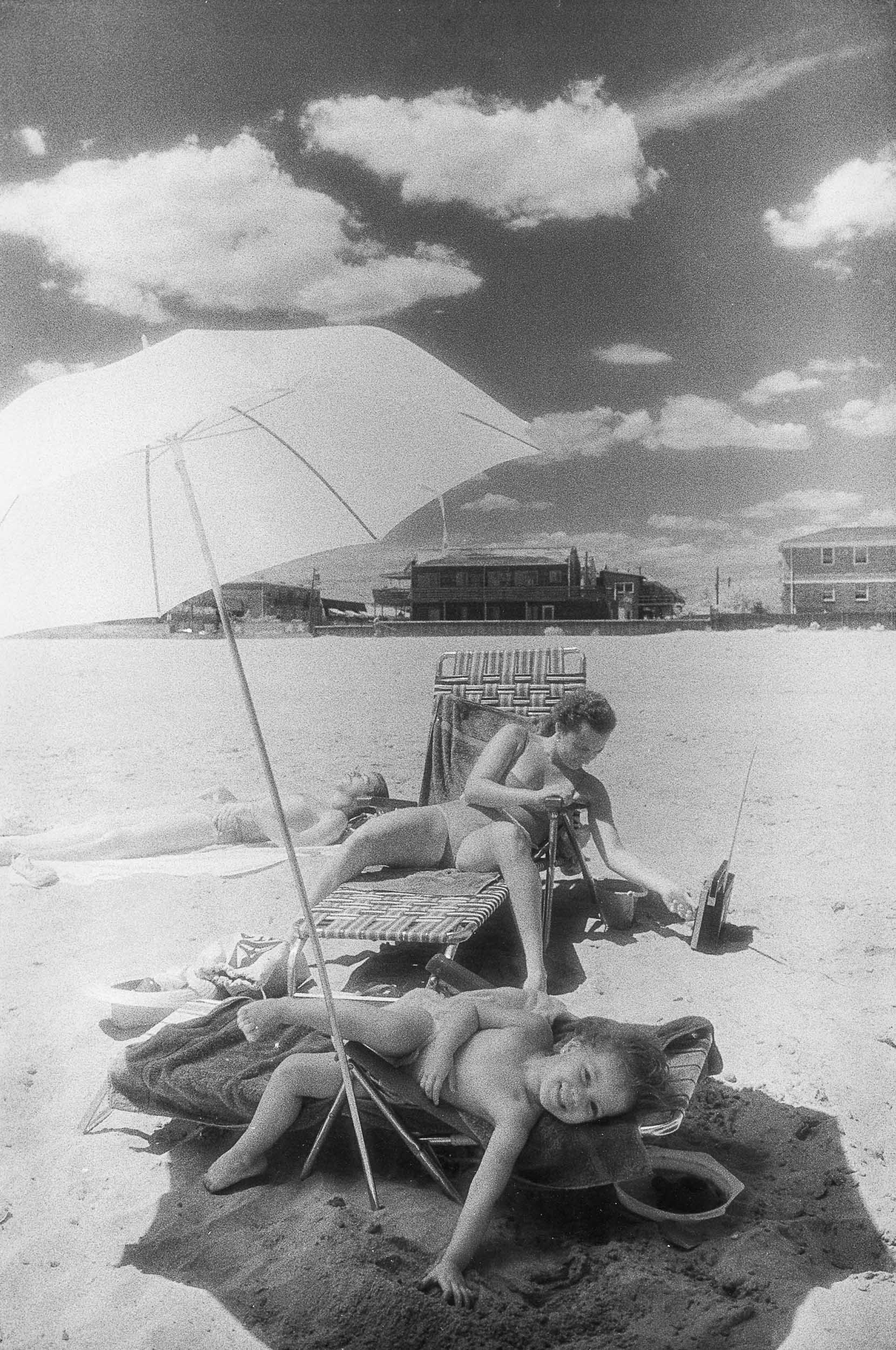 Barbara Alper- Photo of a child lyingunier umbrella  with his mom on Rockaway Beach NYC