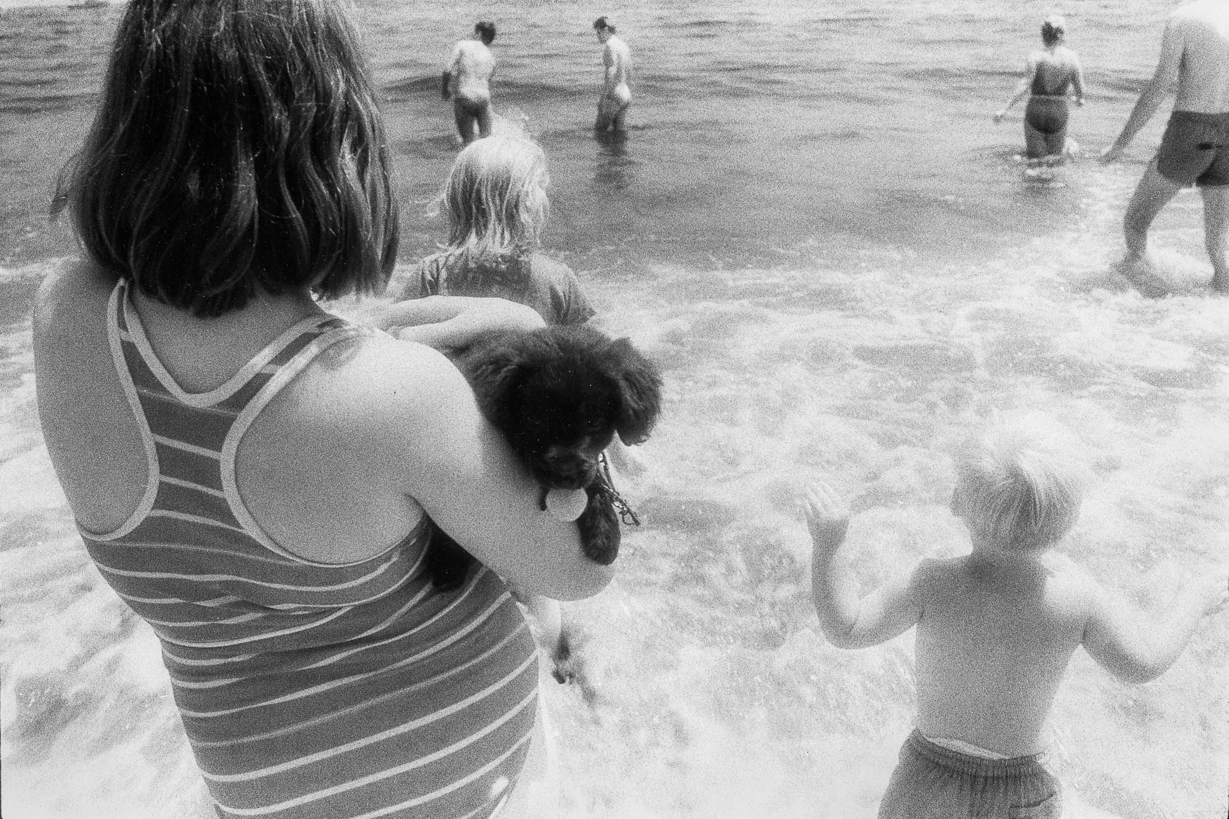 Barbara Alper- Photo of a woman holding a puppy by the ocean with kids at Rockaway Beach NYC