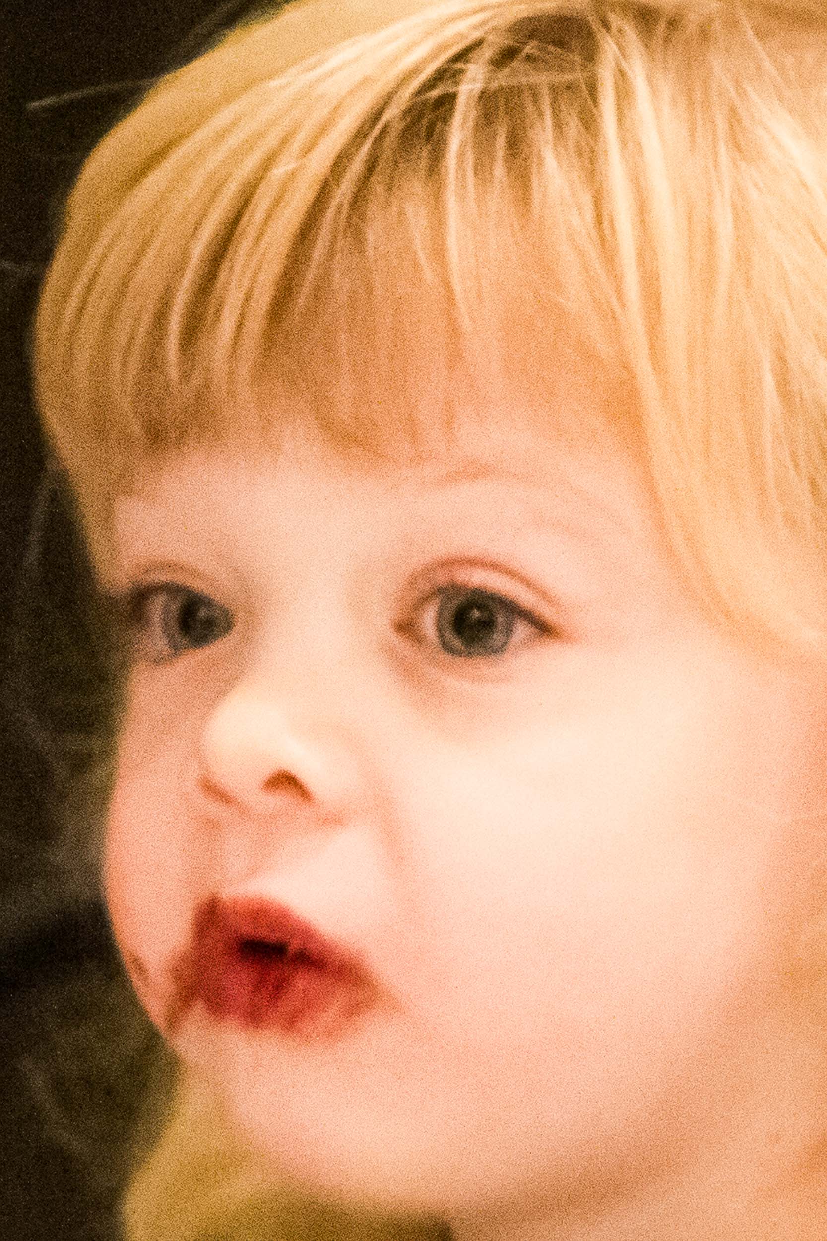 Barbara Alper- Photo of a young blond girl, with round cheeks, red lips and food around her mouth, closeup