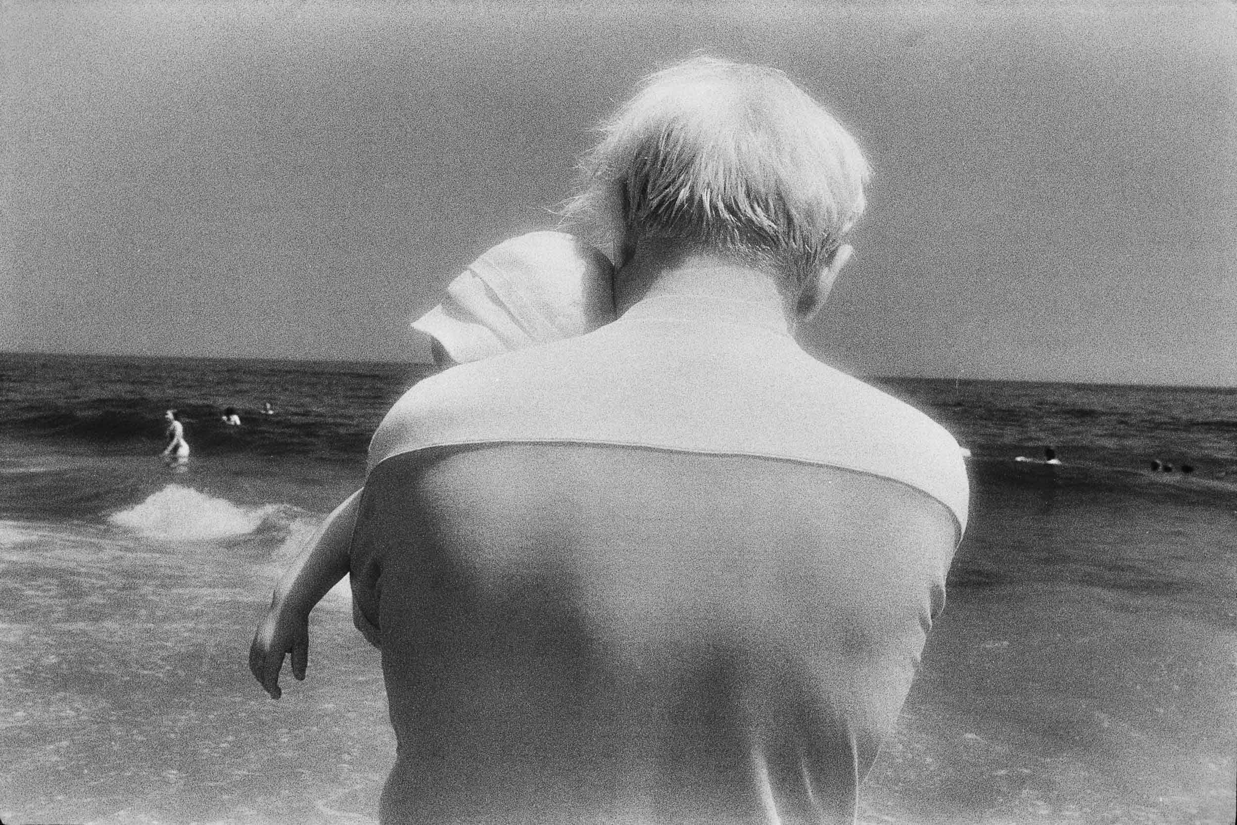 Barbara Alper- Photo of man holding a baby by the water on Rockaway Beach NYC